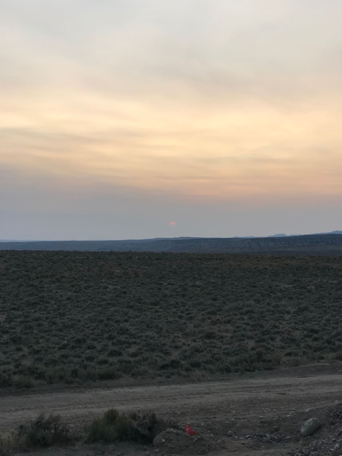 Dusk over the sagebrush basin, the sun a faint disc through haze on the horizon.