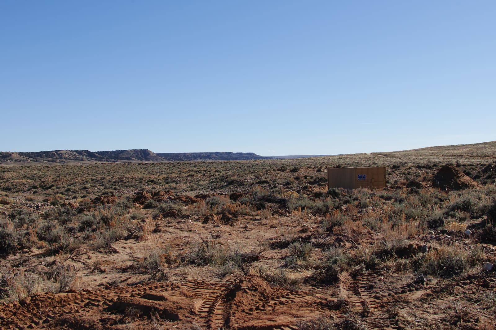A weathered structure alone on the sagebrush plain, with distant bluffs on the horizon.
